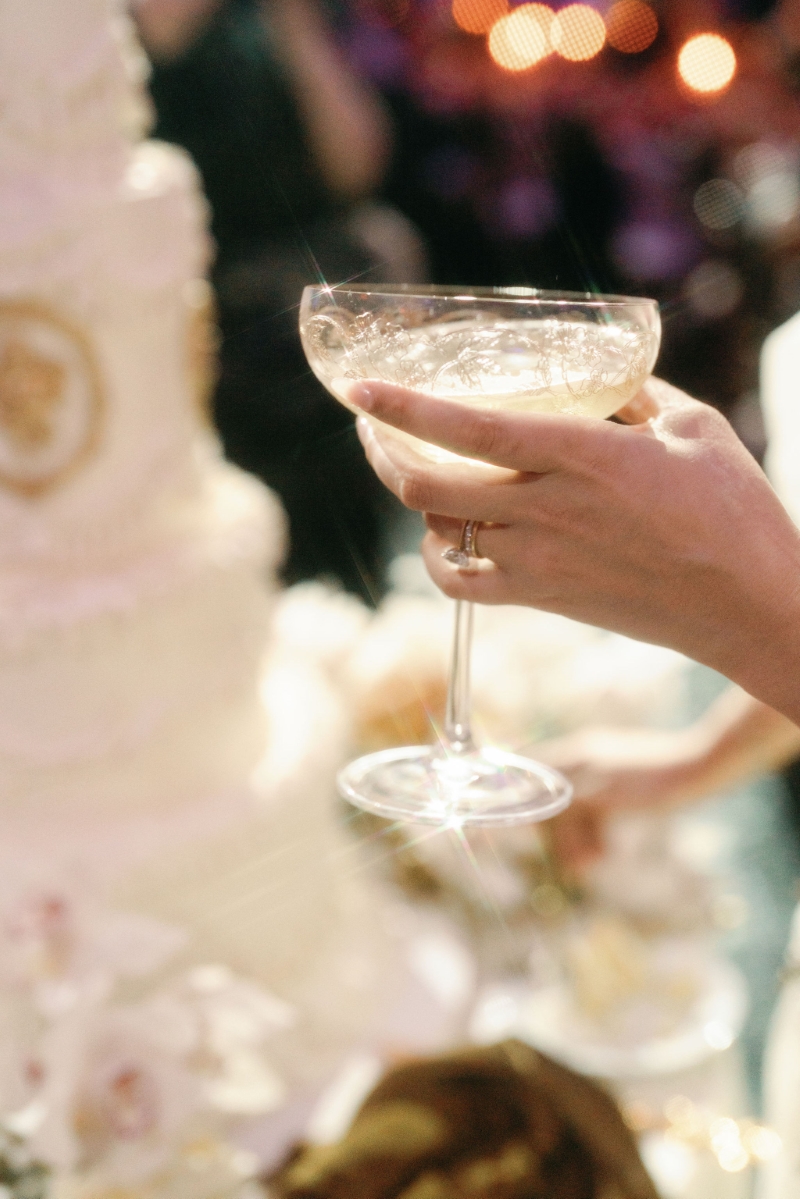 a hand photographed holding a margarita in front of wedding cake