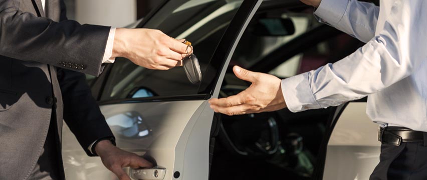 salesman handing new car keys to new car owner