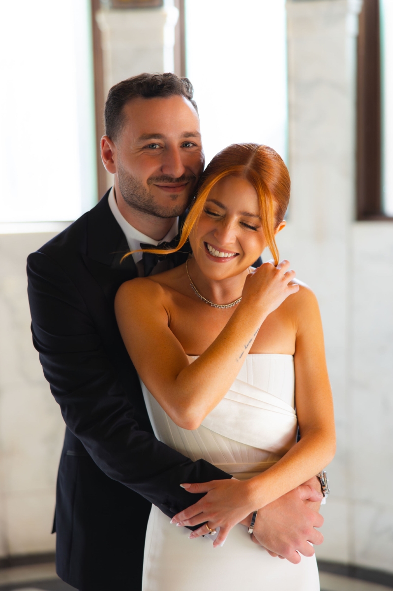 a groom embraces his bride from behind, they're both smiling