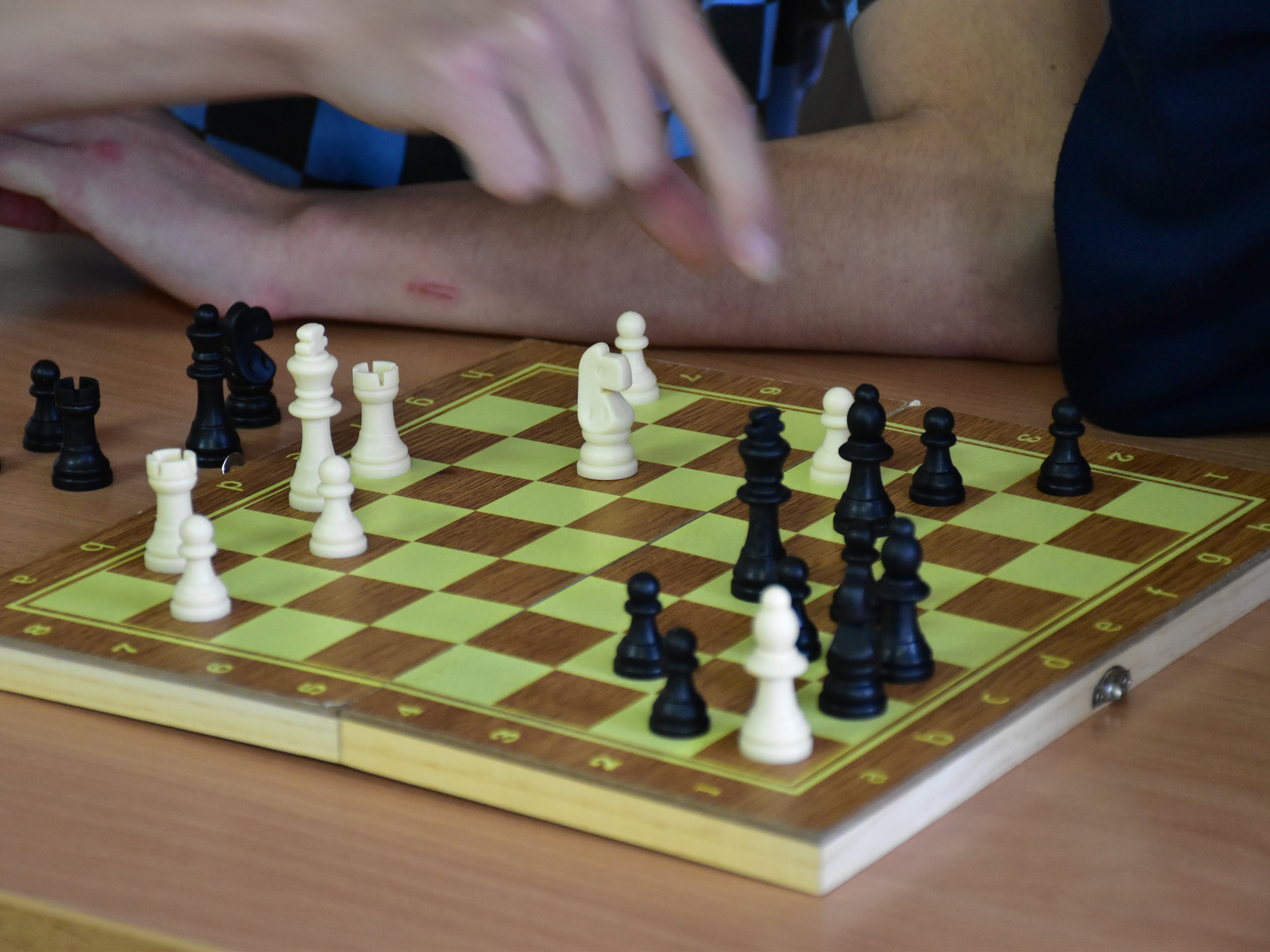 Andrzejkowe wróżby i nie tylko. | Zbliżenie na szachownicę z rozstawionymi szachami w trakcie partii. Nad szachownicą czyjaś dłoń sięgająca po pionek..JPG