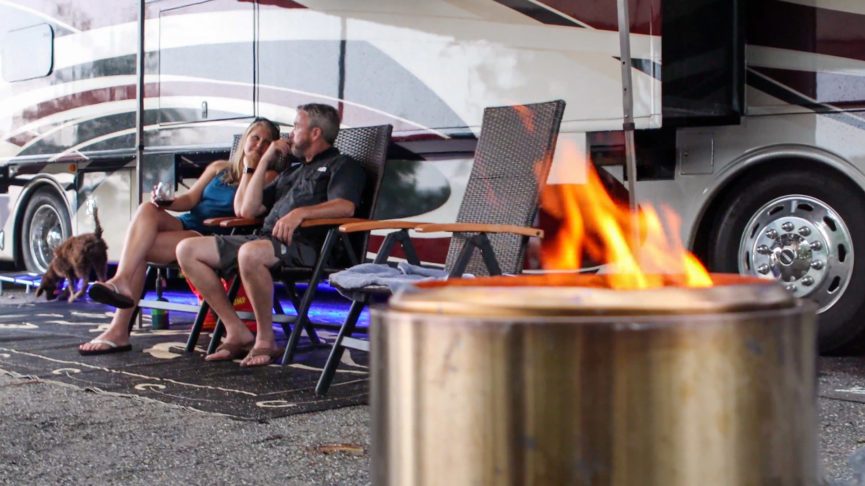 People sitting outside an RV in chairs with a Solo stove going, one of the coolest camping ideas