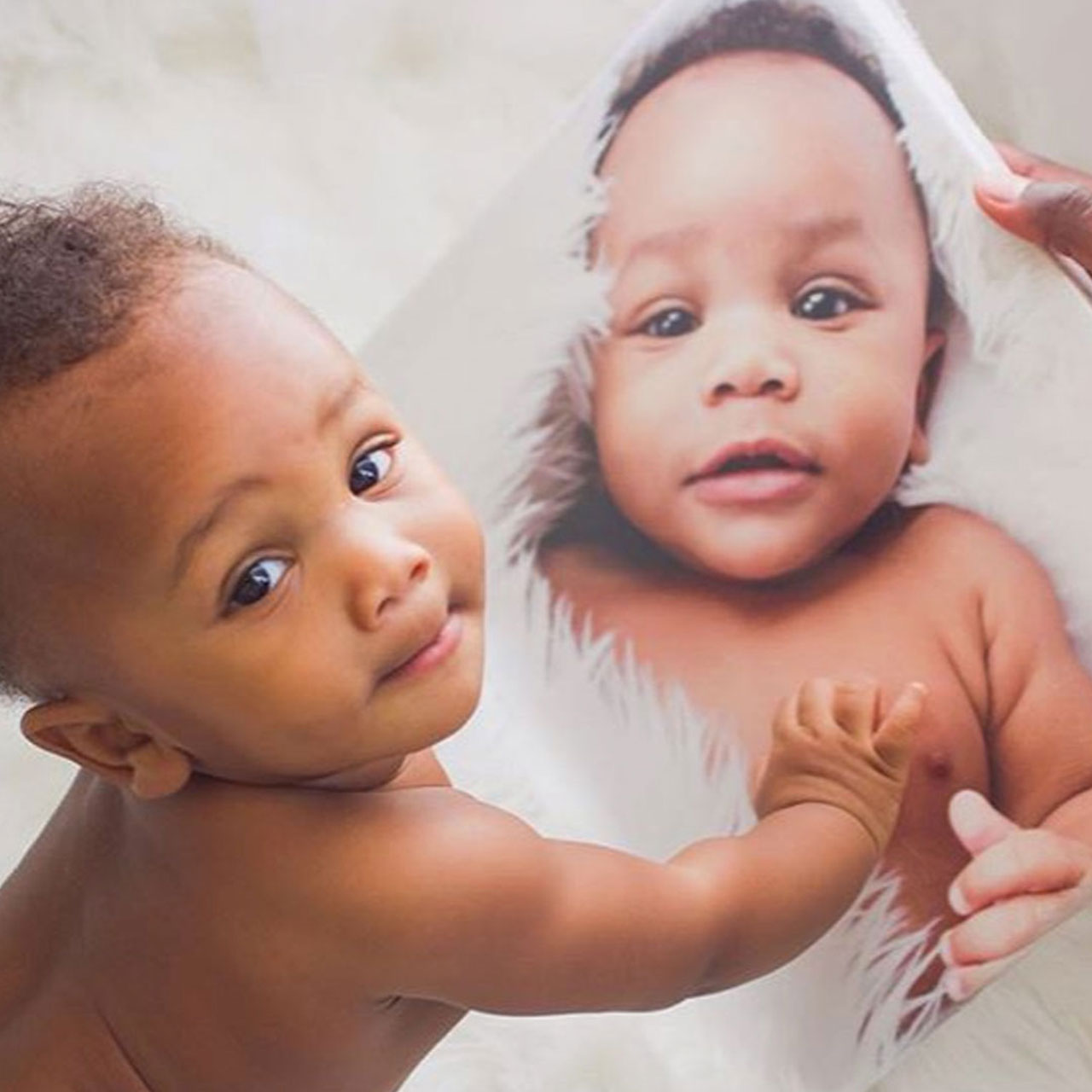 Smiling baby sits next to a canvas print that features photo of himself