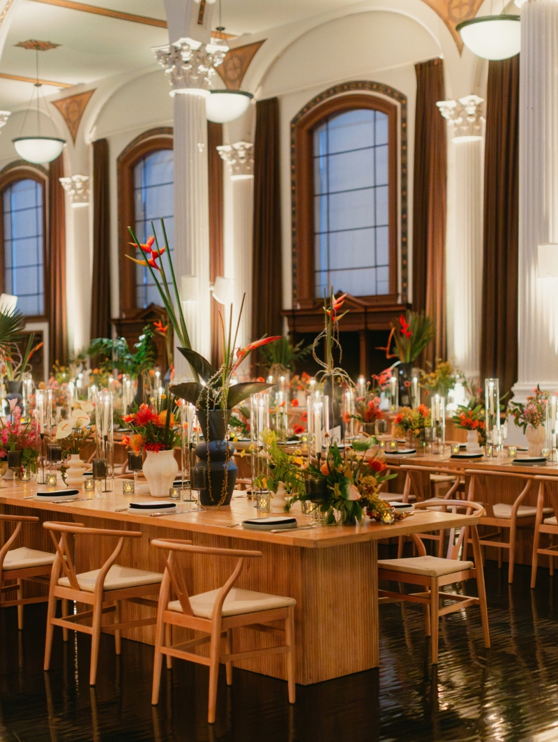 wooden dinner tables in a downtown Los Angeles cathedral wedding reception hall with florals and candles