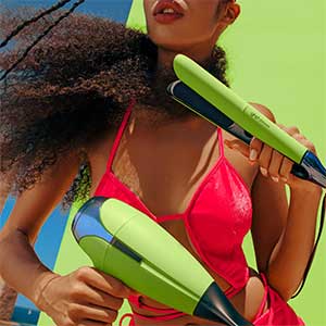 A girl wearing pink holding two hair styling tools - one green straightener and one green hair dryer.