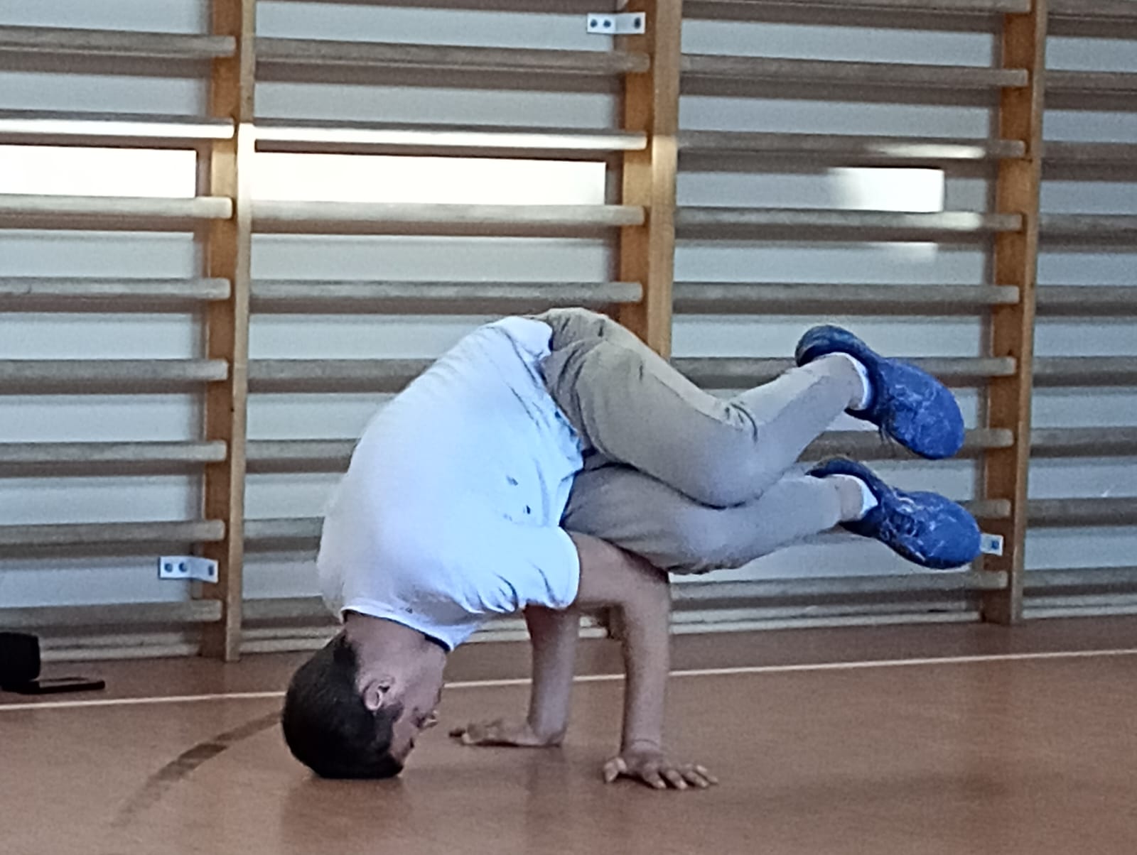 Zajęcia z programu "Fajna ferajna" | Trener tańca pokazując figurę opiera się o podłogę dłońmi i głową, reszta ciała w powietrzu. W tle drabiki sali gimnastycznej..jpg