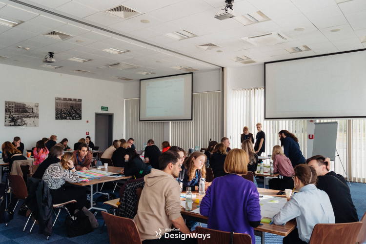 Dozens of Designers in a conference room working in groups on a paper canvas during DesignWays 2022 conference. Author standing in the background.