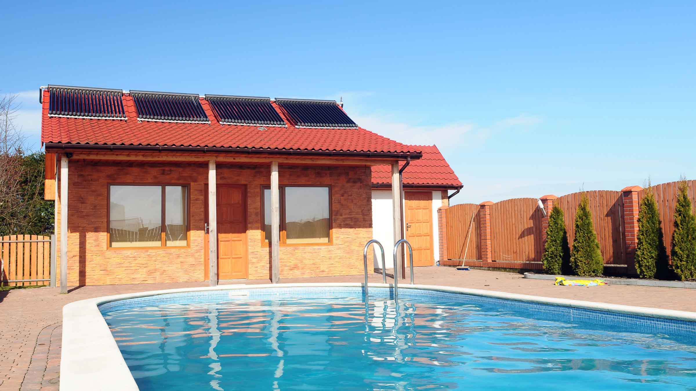Small house with four solar panels on its roof sits at end of pool.