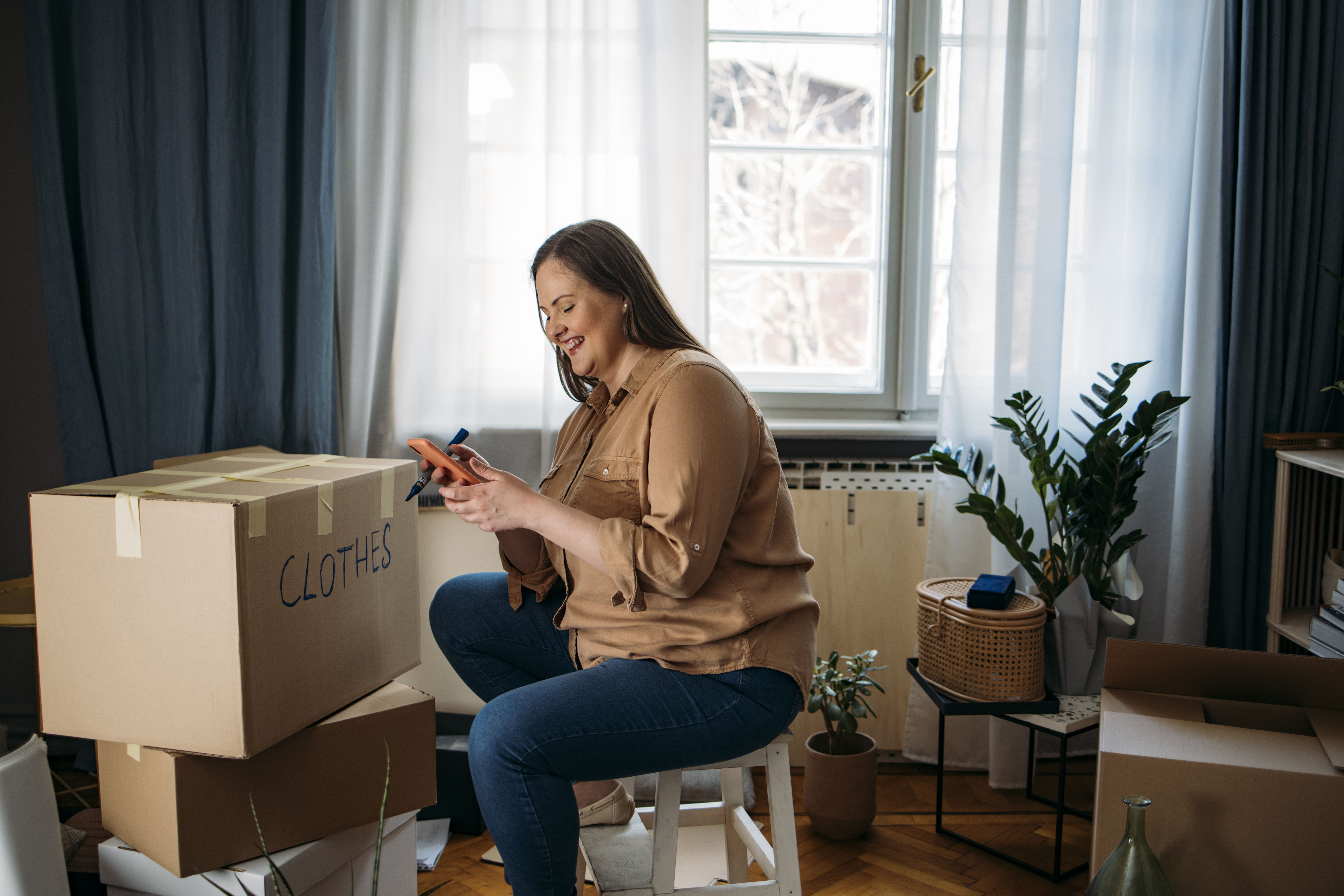 A smiling woman moving out - taking a break from packing and using her mobile phone
