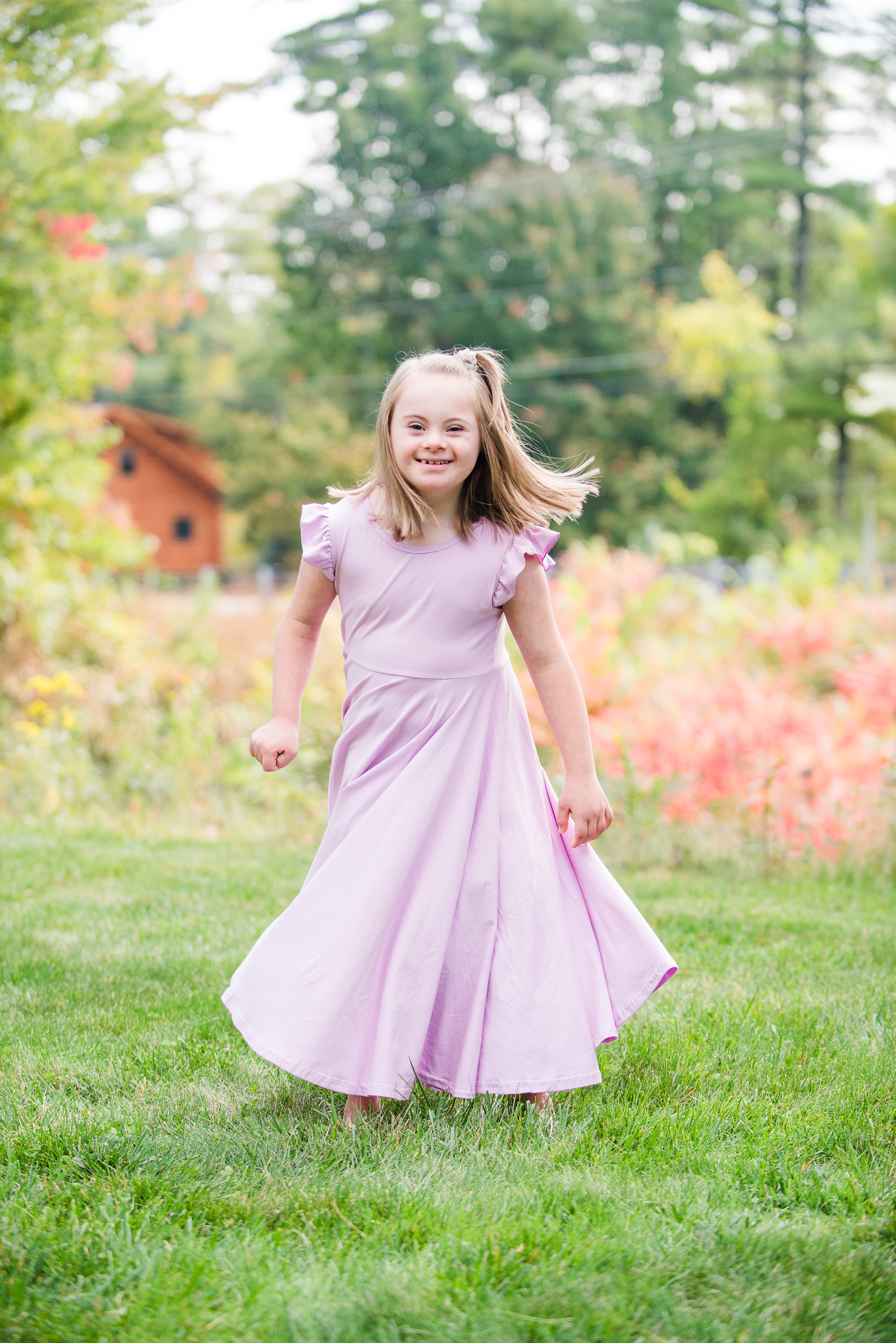 A young girl with down syndrome wearing a pink dress smiling outdoors