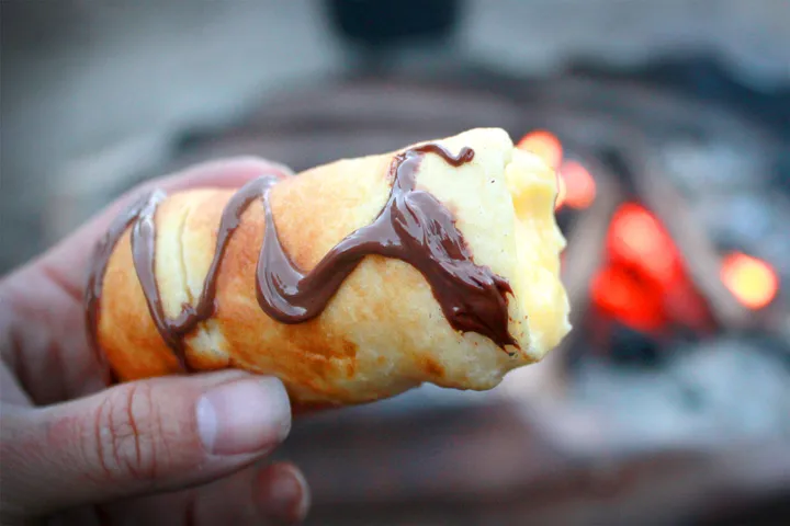 Someone holding a campfire eclair in their hand, one of the best camping ideas
