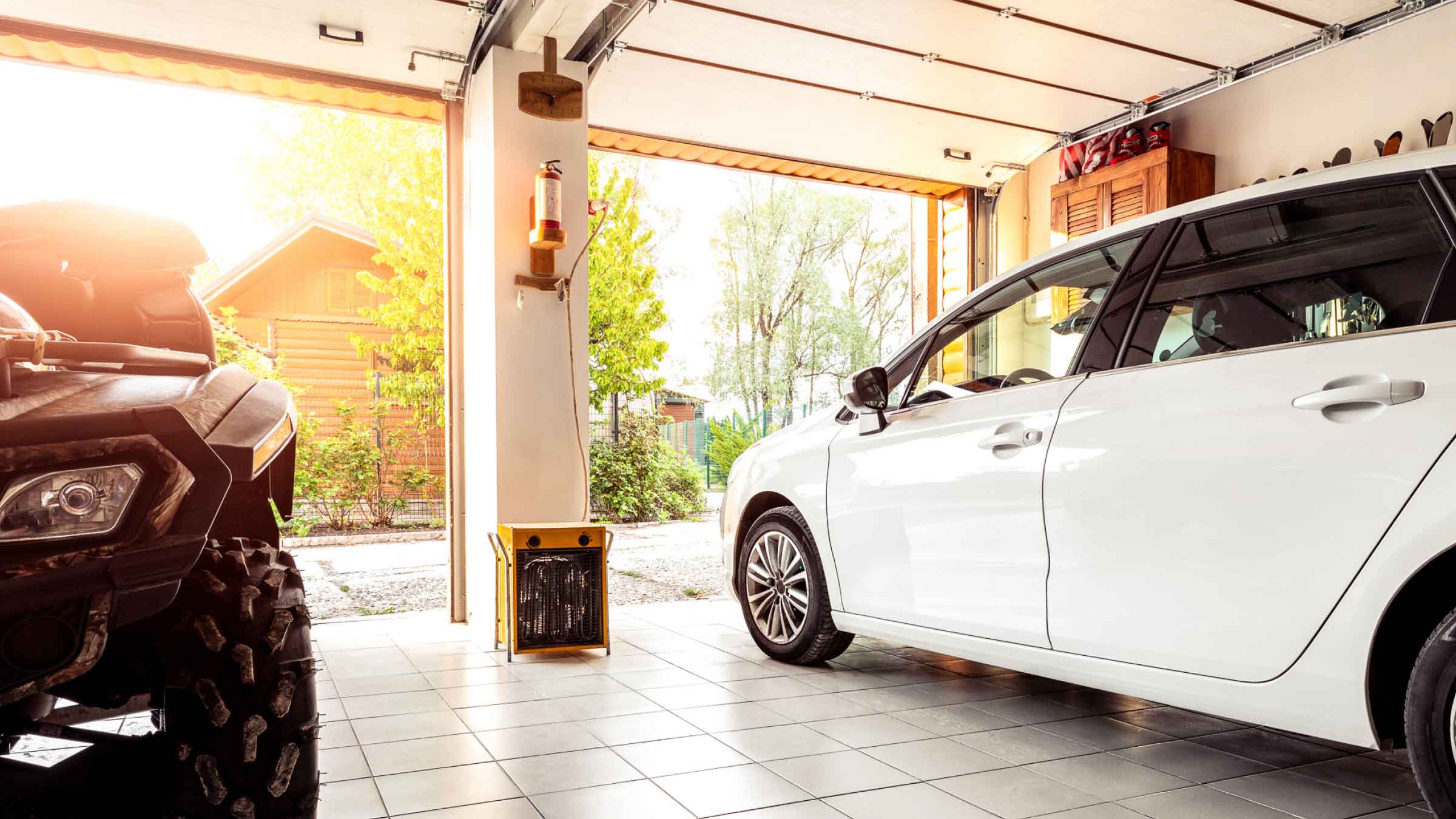 Small white car, parked in a modern well organised garage with open electric roller door.