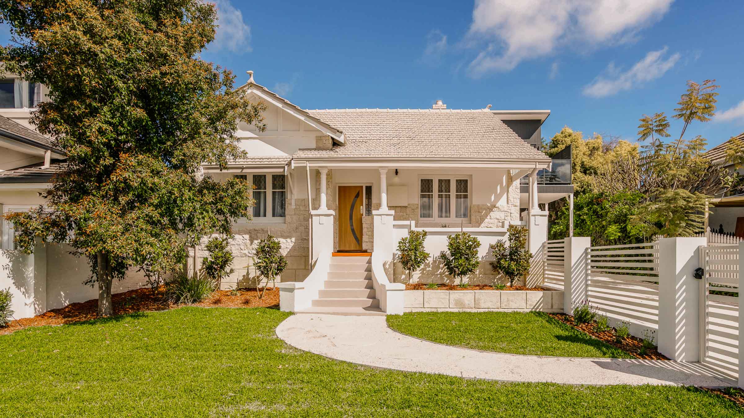 White bungalow with steps leading up to front door. And a beautiful manicured front garden and white wooden fence surround.