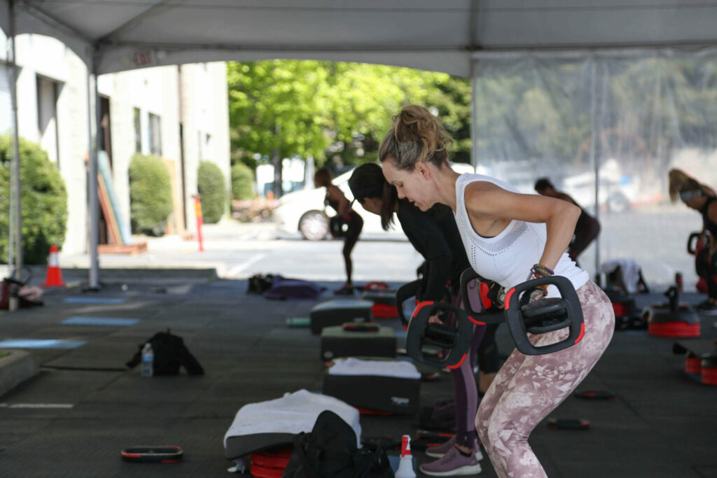 Woman taking group fitness class outside in parking lot of her gym