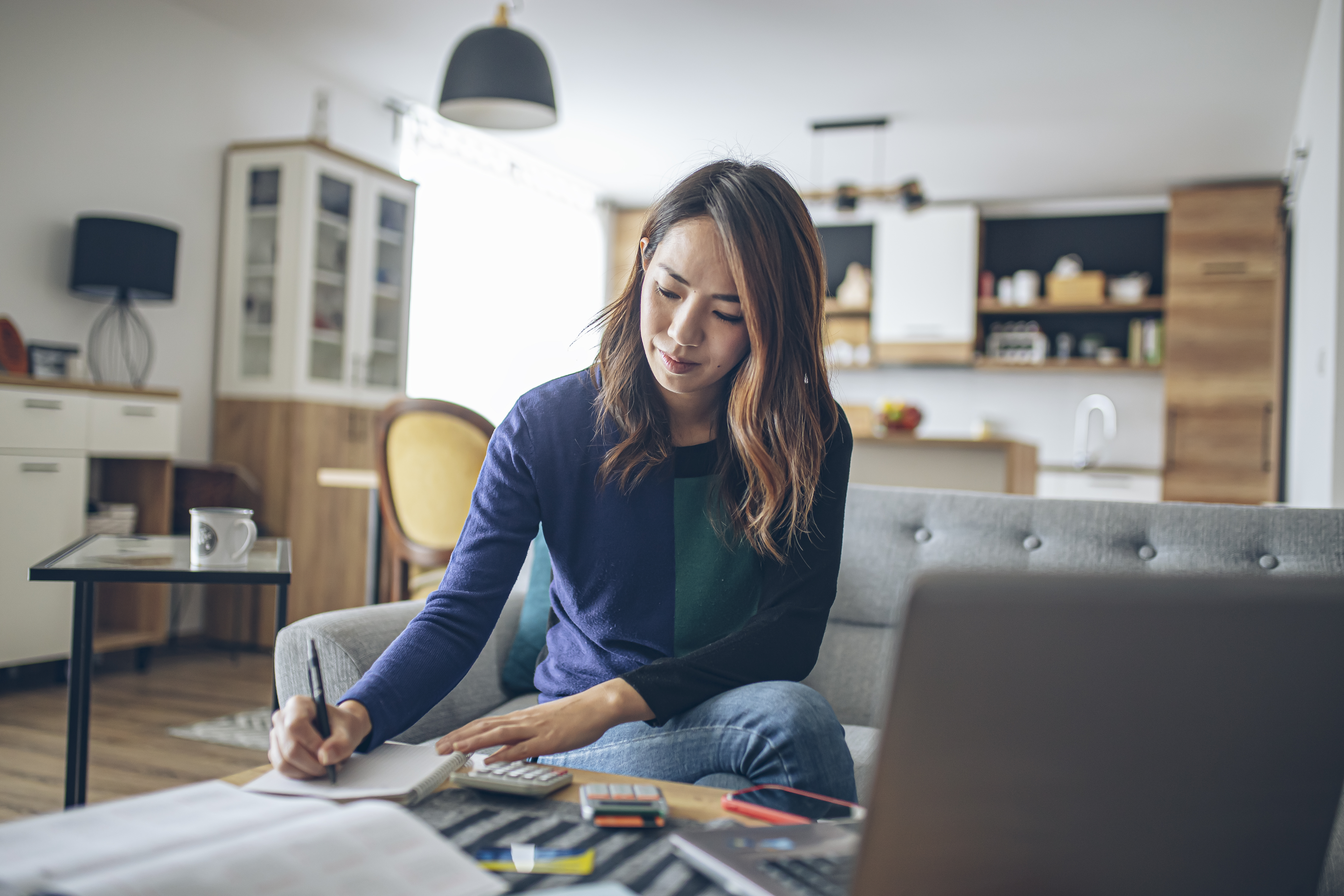 Young woman at home in front of laptop comparing costs with a calculator