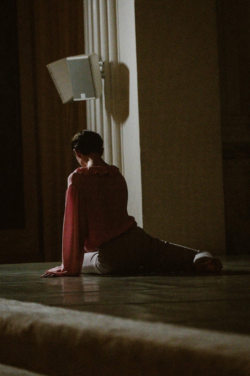 a dancer is sitting on the stage with their back turned toward the camera. the lighting is dim, and the mood is forlorn. at a dance gala at Vibiana in Downtown Los Angeles