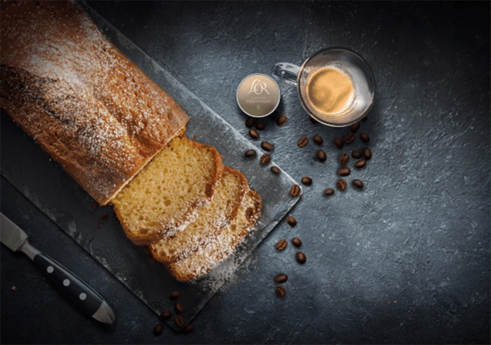 Sliced bread with a cup of L'OR Espresso, accented by scattered coffee beans on a dark surface.