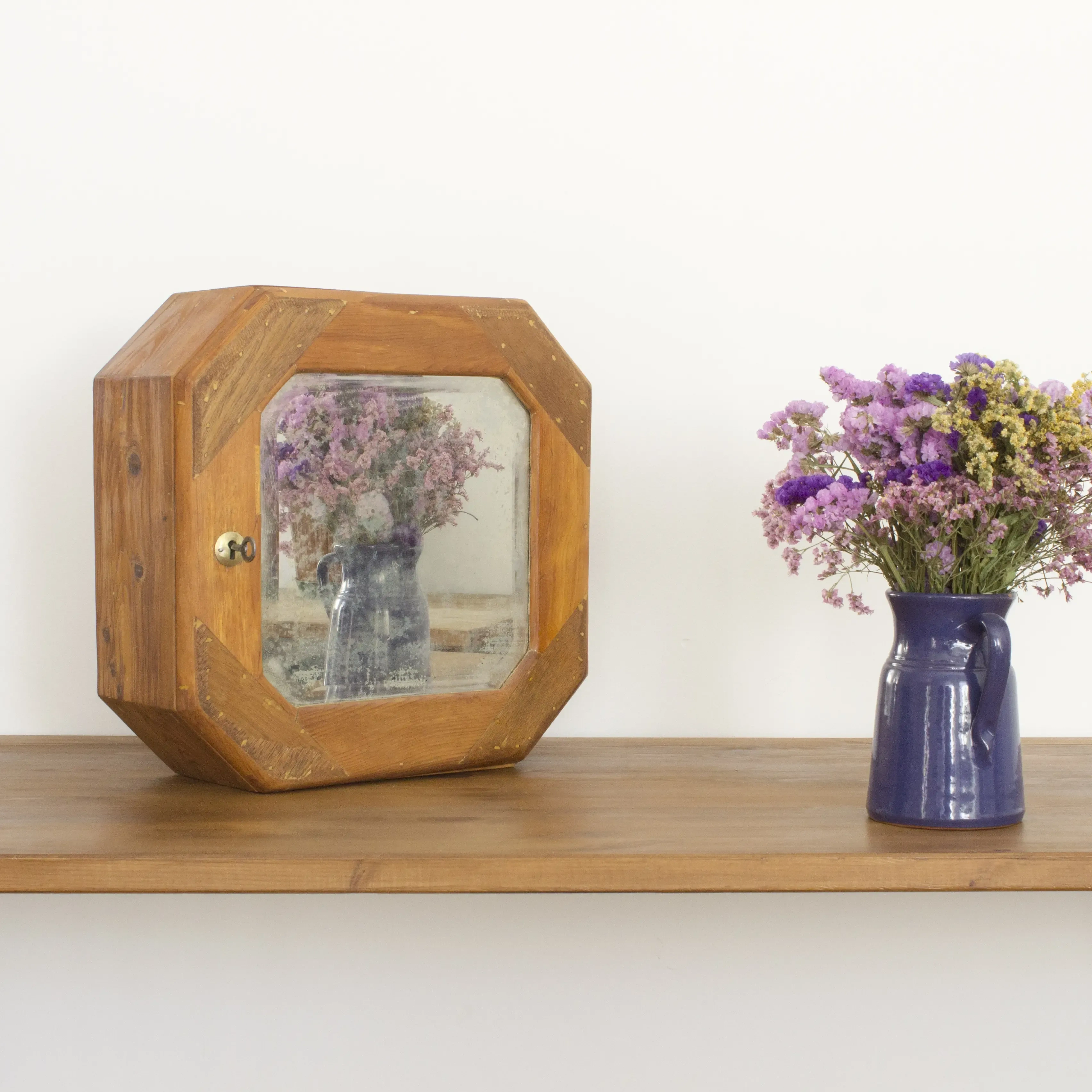 Jarrón con flores junto a botiquín de medicinas de madera con espejo.
