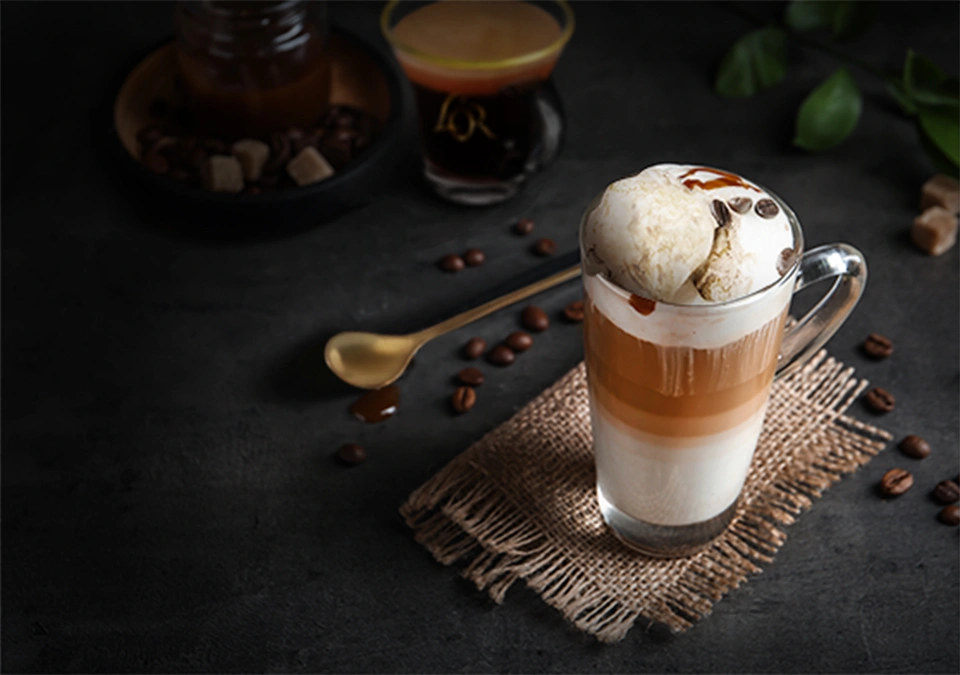 Layered iced coffee with cream and L'OR Espresso, garnished with coffee beans on a dark surface.