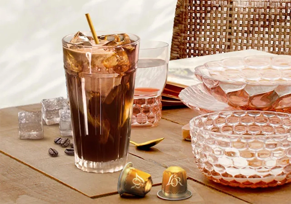 Refreshing iced coffee with L'OR Espresso, served in a glass and accented with a gold straw and capsule assortment.