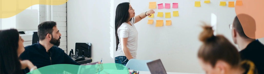 A lady leading a discussion, while showing sticky notes on a whiteboard