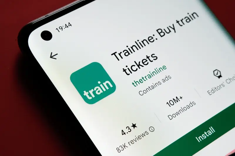 Trainline app seen in Google Play store on smartphone screen placed on red background