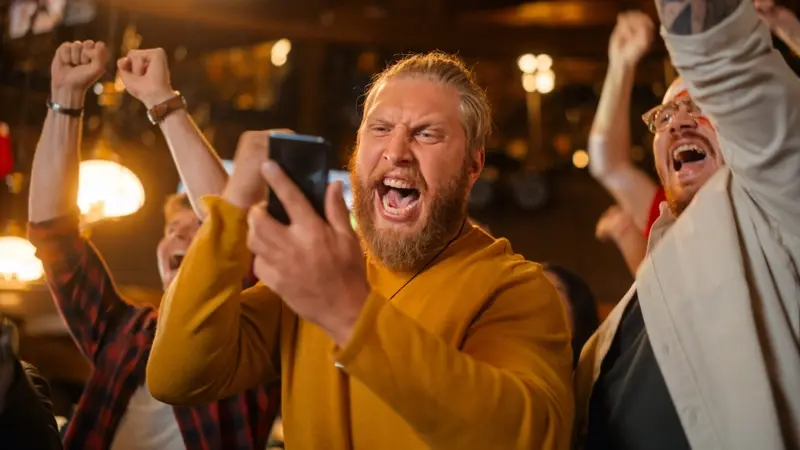 Man in pub celebrating sports bet win with phone in hand