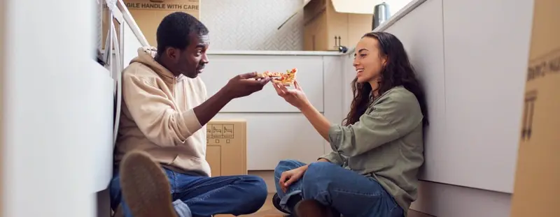 young couple surrounded by moving boxes eating pizza on the floor 