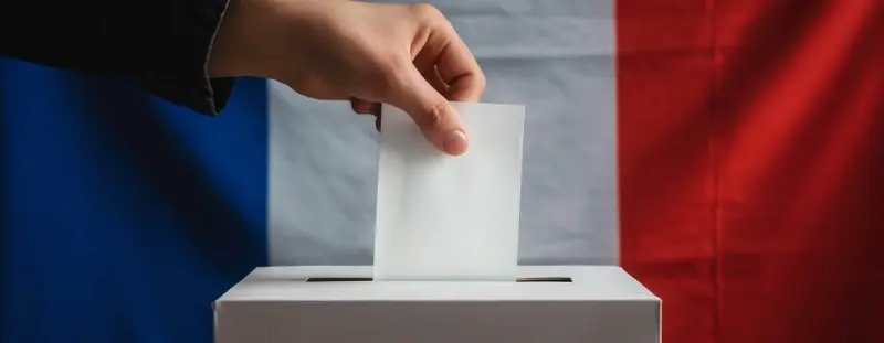 Someone placing a polling card in a box with a French flag in the background