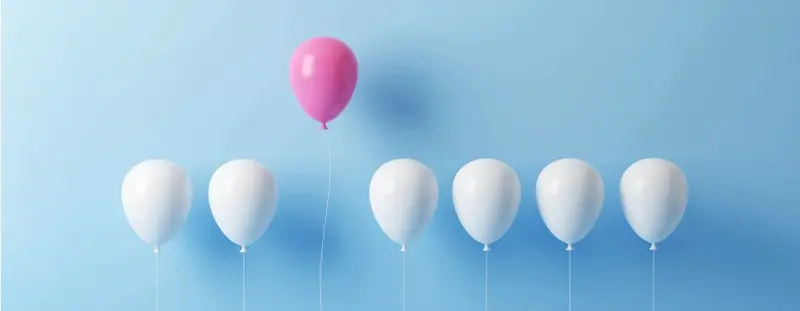 6 white balloons with one pink balloon rising above them 