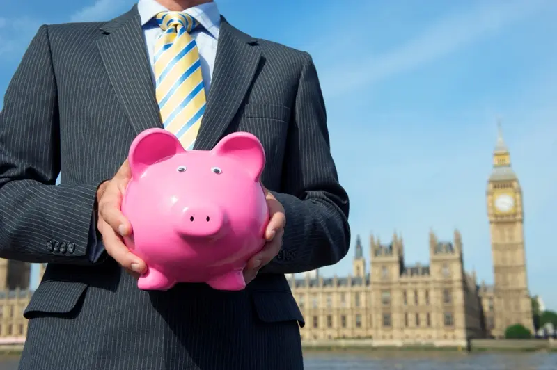 Man holding piggy bank in front of Westminster