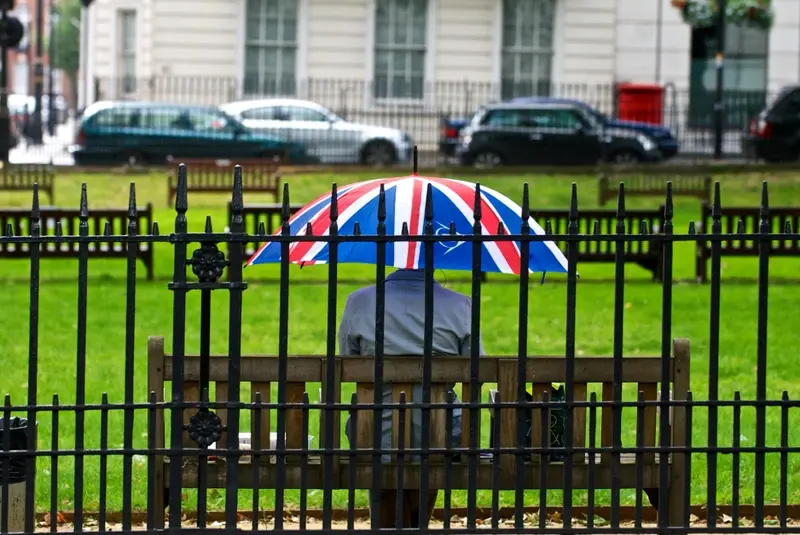 A man sitting in a park with a union jack umbrella