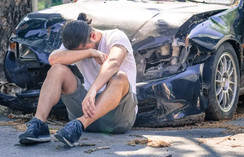 Man sitting in front of a car which has been in an accident