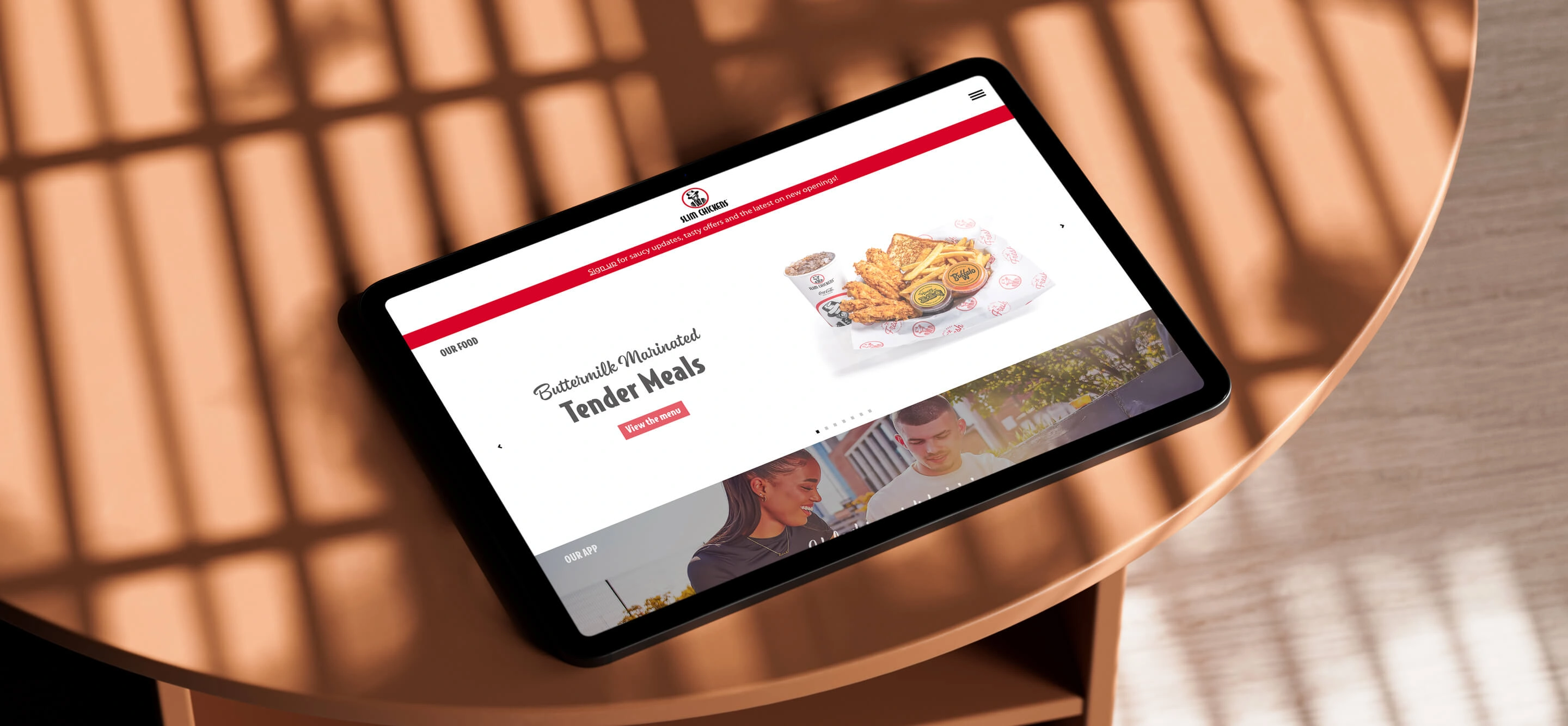 A tablet screen lying on a table showing the Slim Chickens home page
