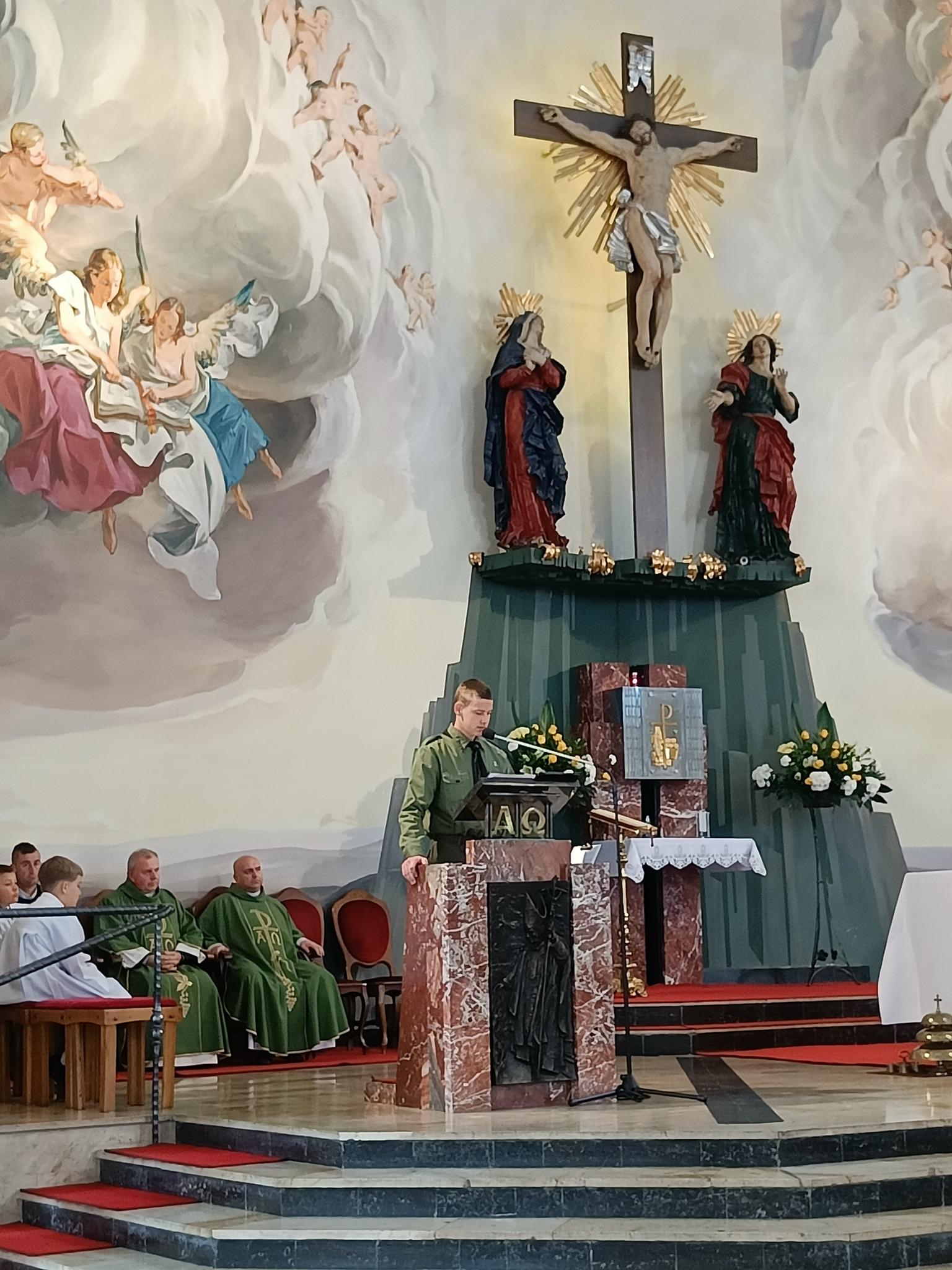 Dzień Papieski | Wychowanek MOW w harcerskim mundurze podczas mszy w kościele czyta za pulpitem na ołtarzu. W tle ołtarz - krzyż, figury, freski, obok siedzą księża w ornatach i ministranci..jpg