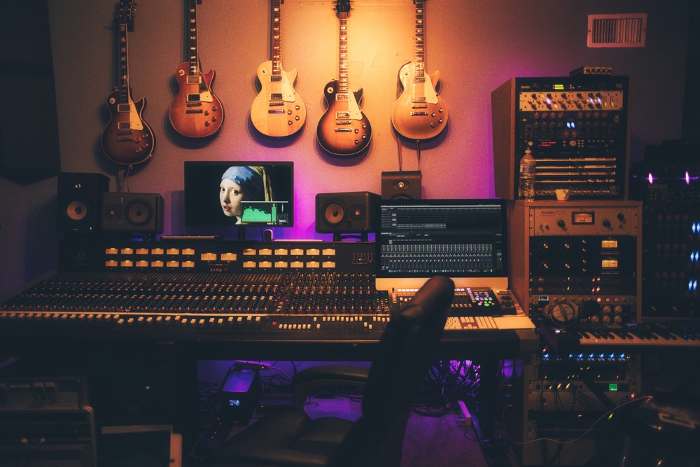 a music production desk with a lot of tools, like computers, consoles, guitars on the wall etc