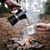 hands pouring tea in a forest with a camping fire