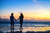 a couple walking down a beach holding hands during a sunset