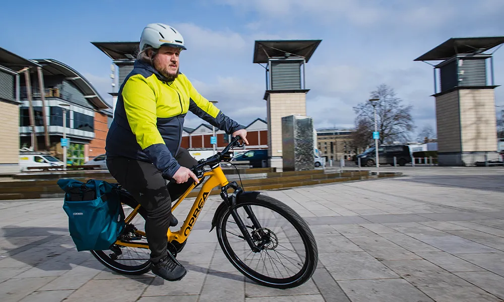 A man rides a yellow electric urban bike past a fountain