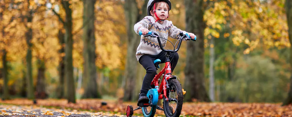 Child riding a bike with stabilisers on an autumn day