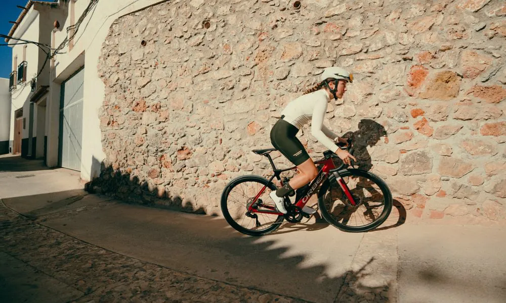 A woman rides an electric road bike past a stone wall