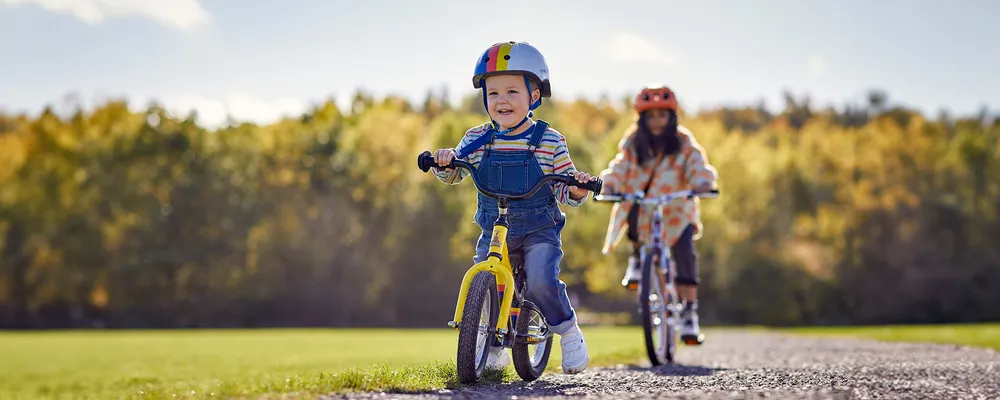 young child riding a balance bike with older child riding behind