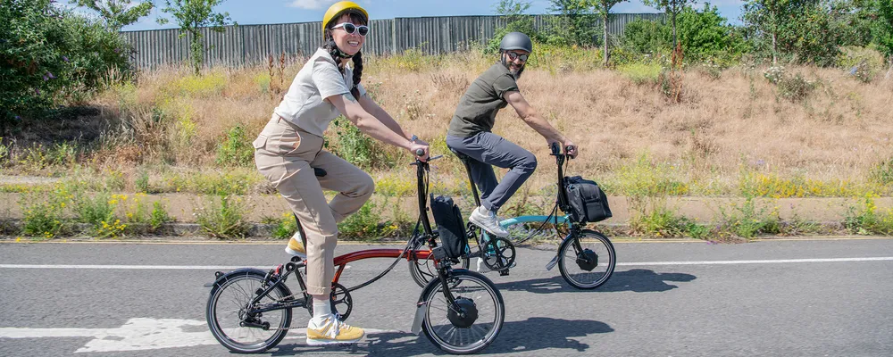 two people riding Brompton electric folding bikes in the sun