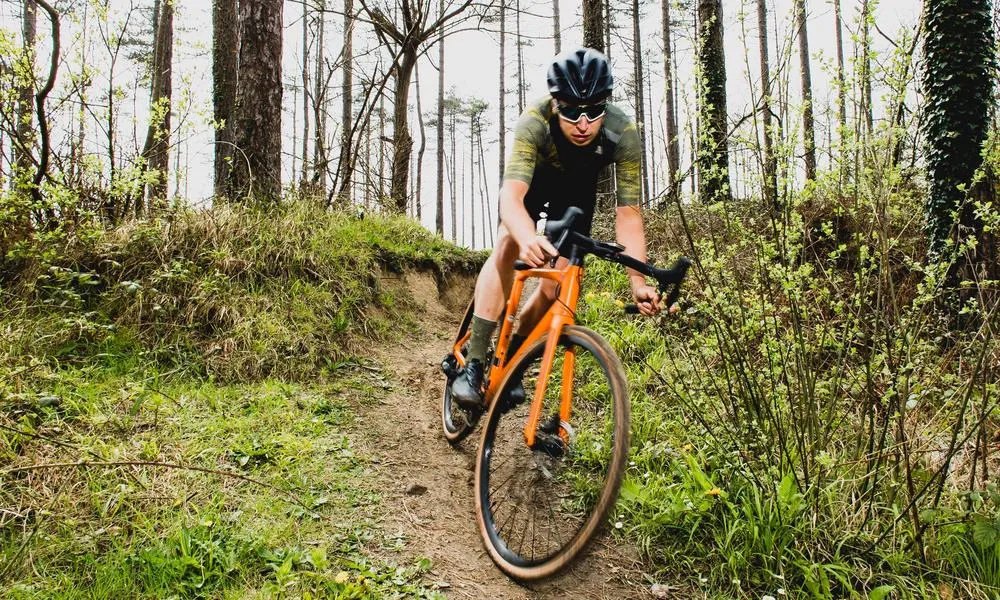 Gravel cyclist riding a singletrack turn in open woodland