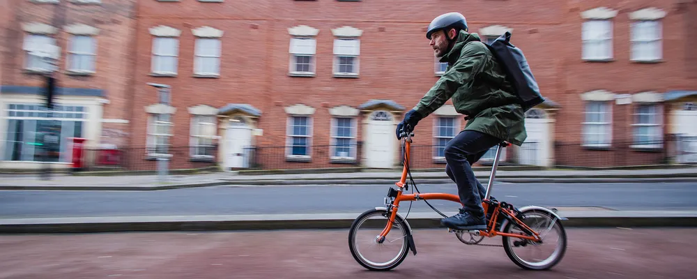 a folding brompton bike is ridden past a red brick building