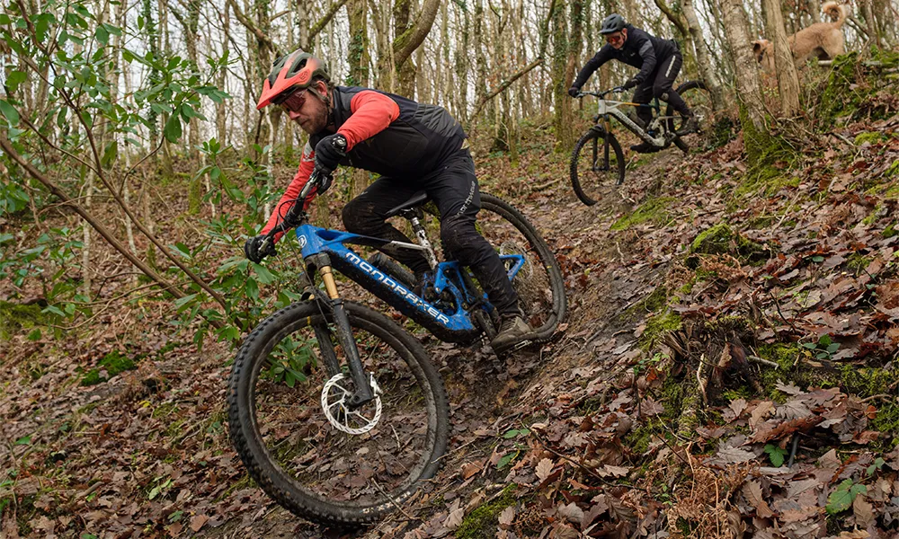 Two electric mountain bikes being ridden downhill in the woods