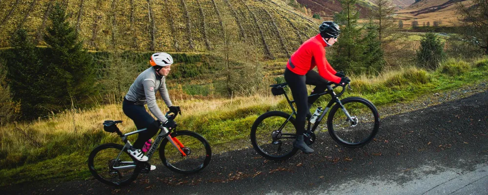 two cyclists riding up a hill in winter