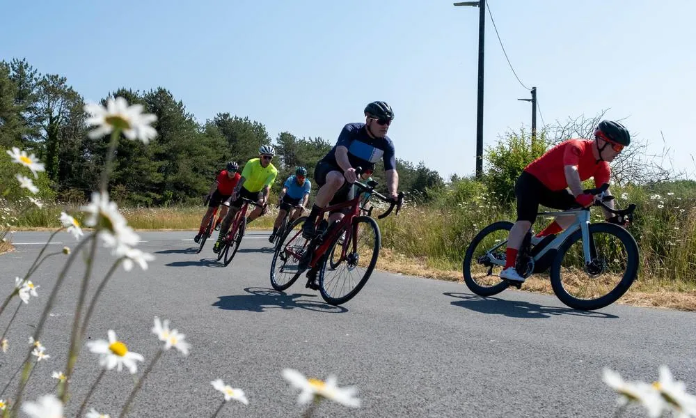 road cyclists cornering in a bunch on  a sunny day with flowers