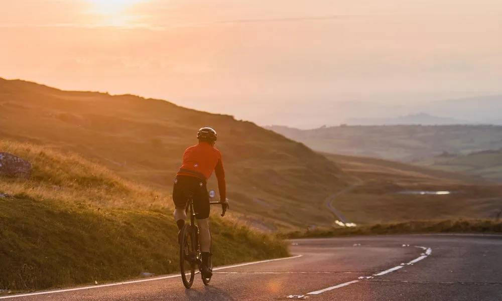 Cyclist descending road at sunset in the Welsh hills