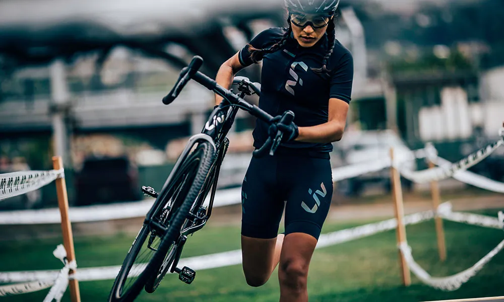 A woman carries a cyclocross bike mid race