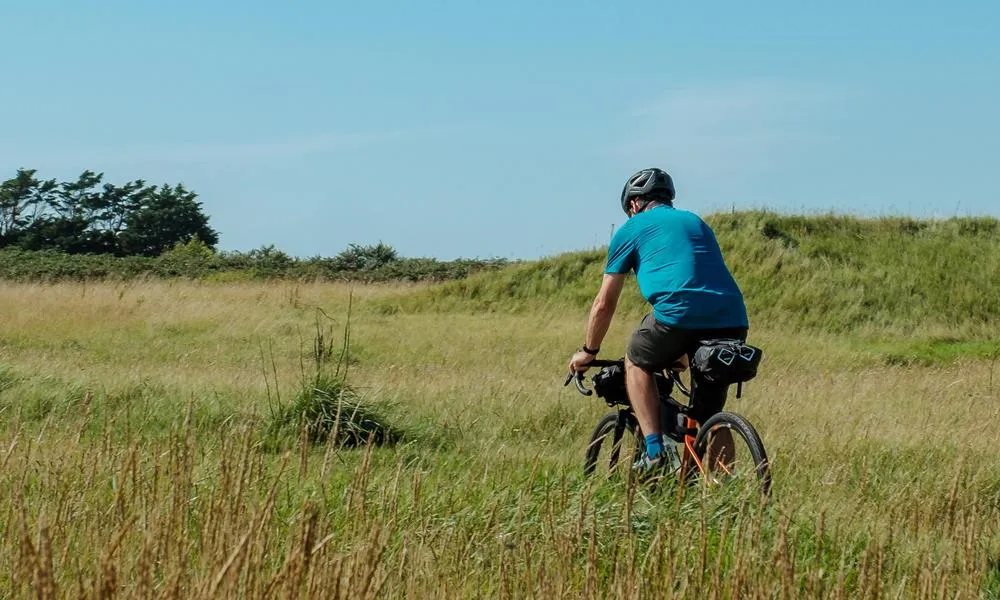 Gravel rider cycling through a grassy field in summer